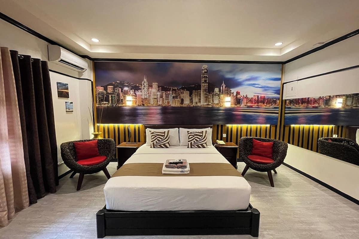 A hotel room with a large bed, two armchairs, a nightstand, and a cityscape mural on the wall.