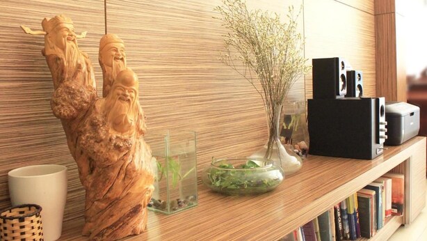 Een houten plank met een beeldje, een vaas met takken, een glazen schaal met planten en een zwarte speaker.