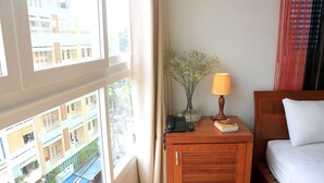 Een hotelkamer met een bed, een nachtkastje met een lamp, een vaas met bloemen, een telefoon en uitzicht op gebouwen door een raam.