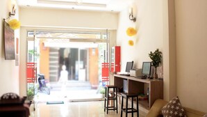 Een moderne hotellobby met een receptiebalie, zithoek en uitzicht op de straat.