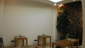 Een moderne eetruimte met houten tafels en krukken, een grote potplant en een stenen muur.