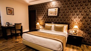 Una habitación de hotel con una cama grande, dos mesitas de noche con lámparas, un escritorio con una silla y una pared con papel tapiz estampado.