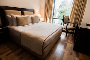 A neatly made bed with a headboard, a bedside table with a lamp, a chair, and a desk.