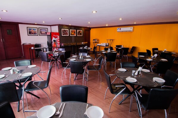 A dining area with multiple tables and chairs, a Coca-Cola refrigerator, and framed pictures on the wall.