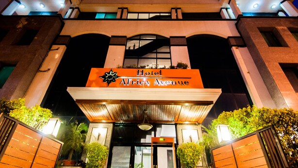 Exterior del Hotel Africa Avenue de noche, con un letrero llamativo, una entrada imponente con toldo y alrededores bien iluminados.