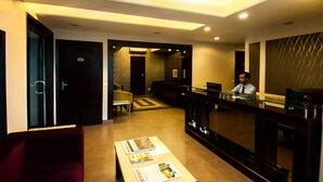 Un vestíbulo de hotel con una recepción, una zona de estar y una escalera que sube a otro piso.