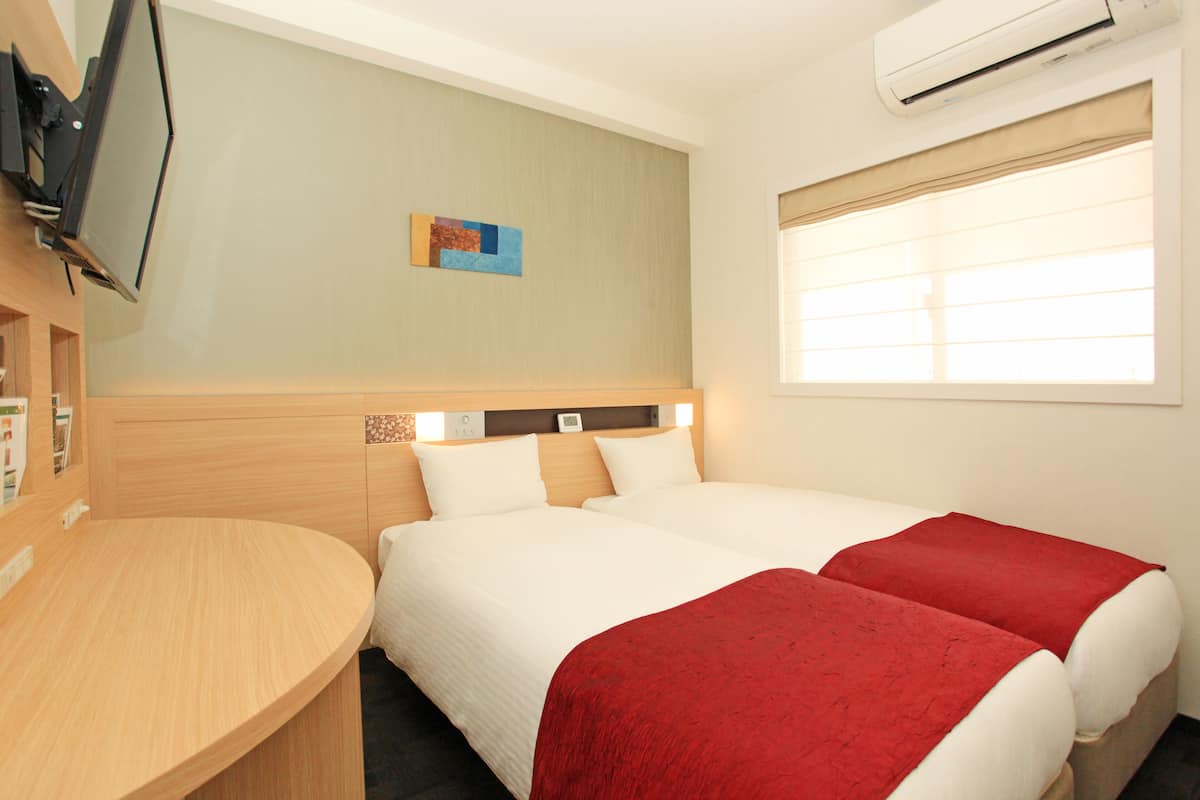 Une chambre d’hôtel avec deux lits, une télévision, un climatiseur et une fenêtre avec des stores.