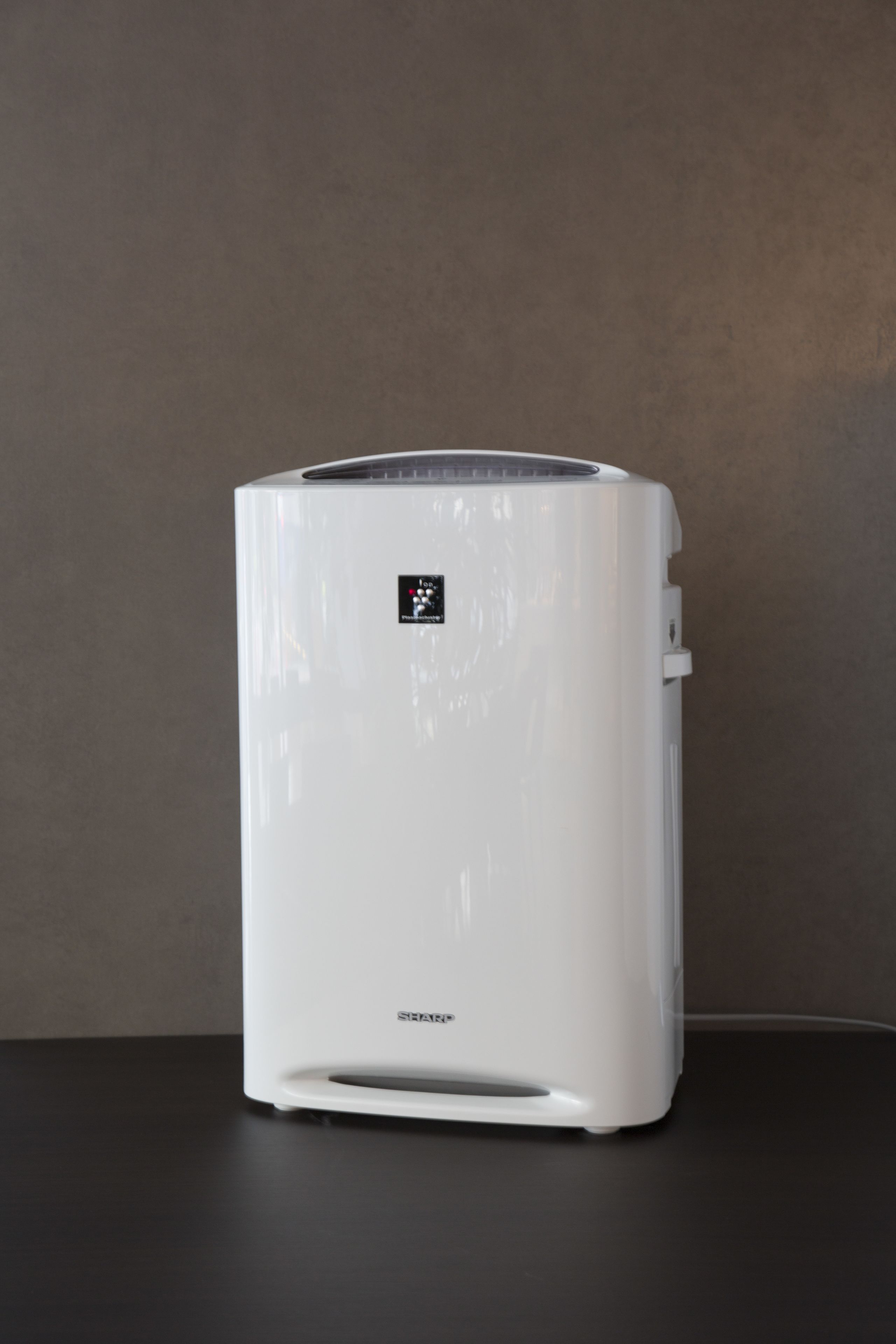 A white air purifier with a digital display on a dark surface against a plain wall.