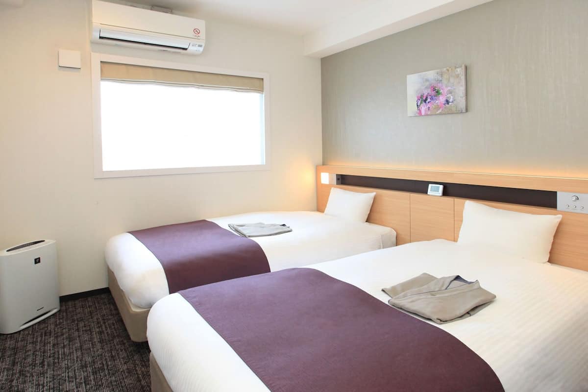 Une chambre d’hôtel avec deux lits, une fenêtre, un appareil de climatisation et un tableau au mur.