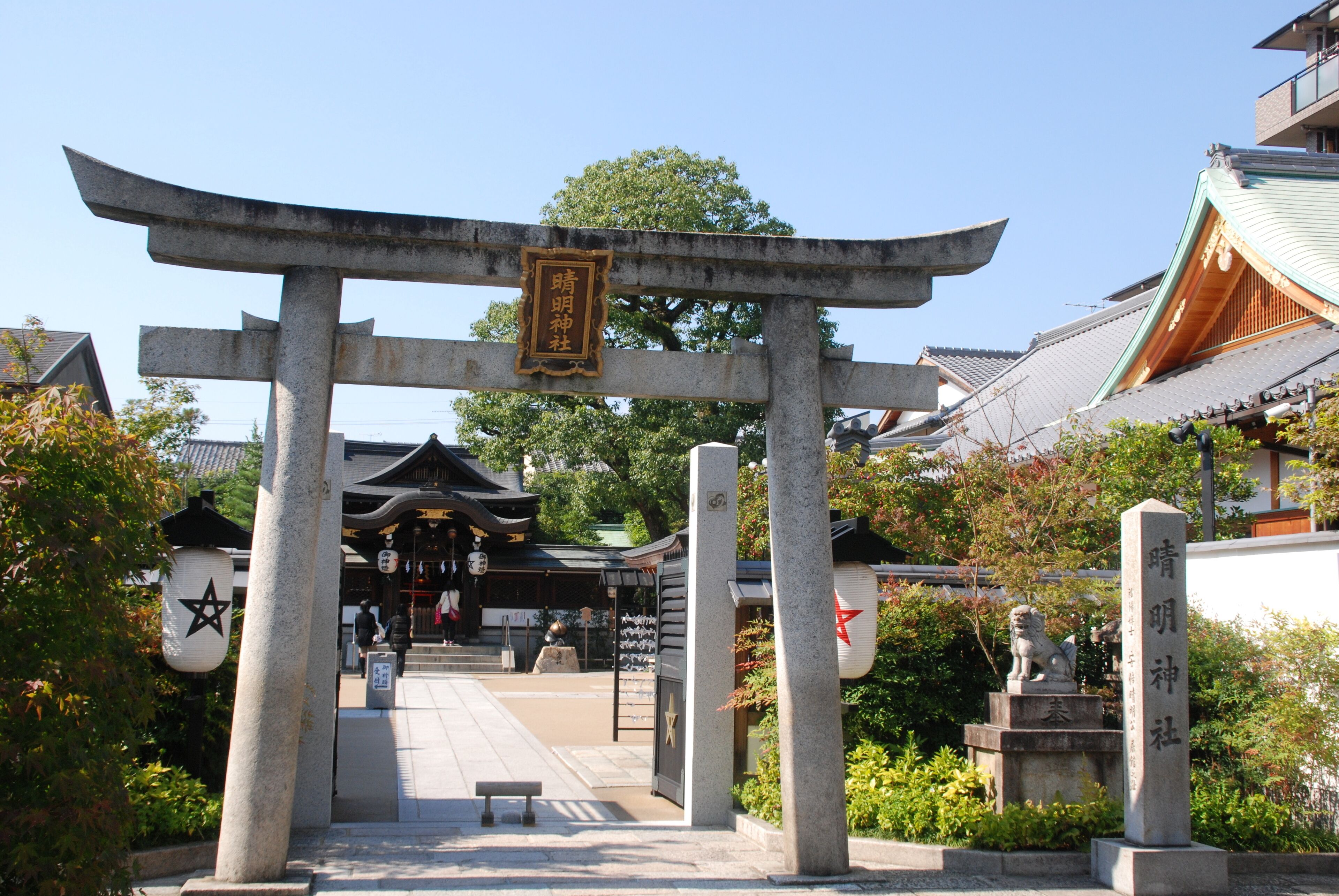 A traditional Japanese torii gate leading to a temple complex with a stone lion statue in front.