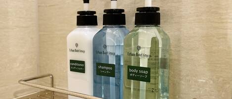 Uma prateleira no banheiro com três frascos de produtos de higiene do hotel: condicionador, shampoo e sabonete líquido.