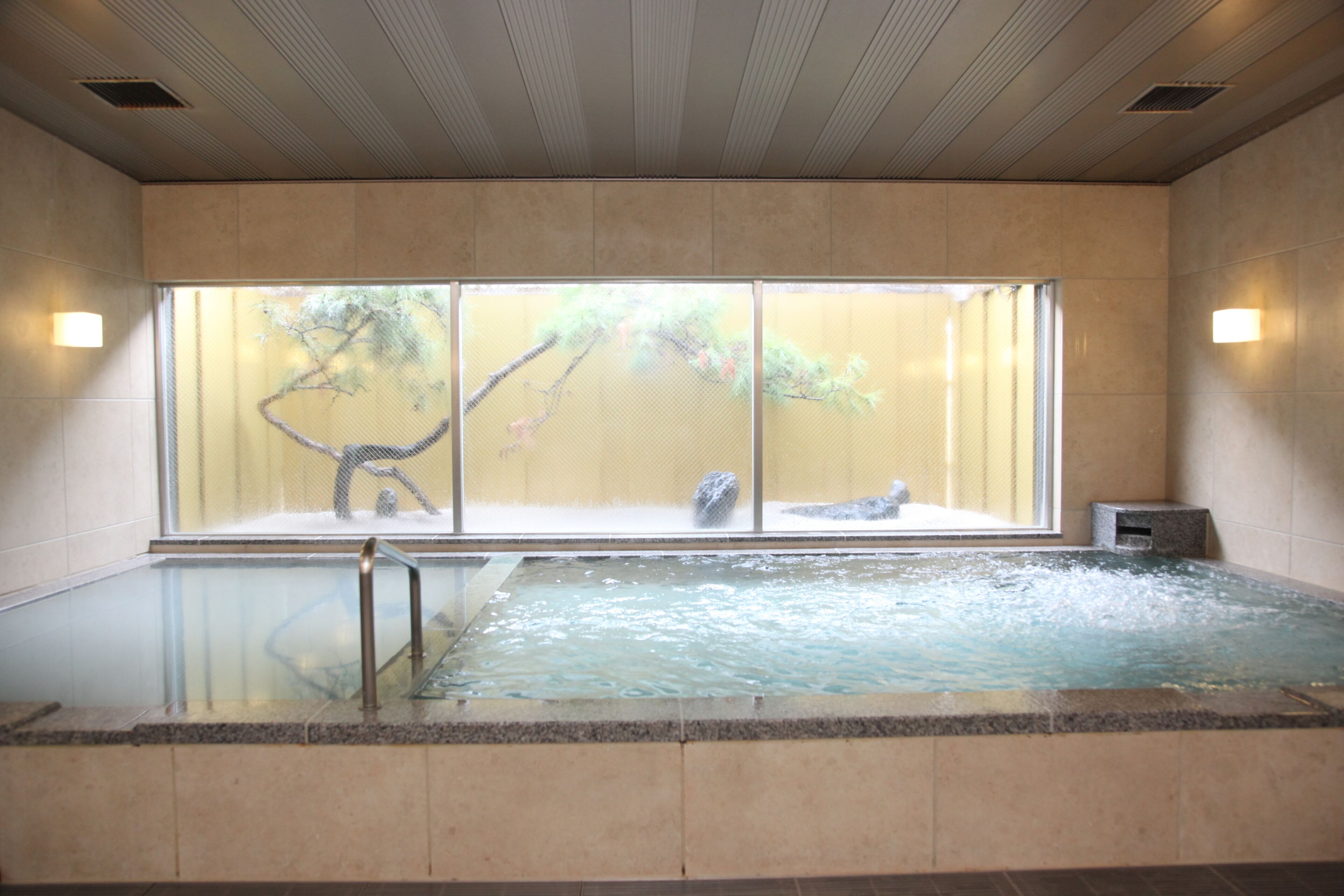 A spa with a large indoor pool, a view of trees through a window, and a stone bench.