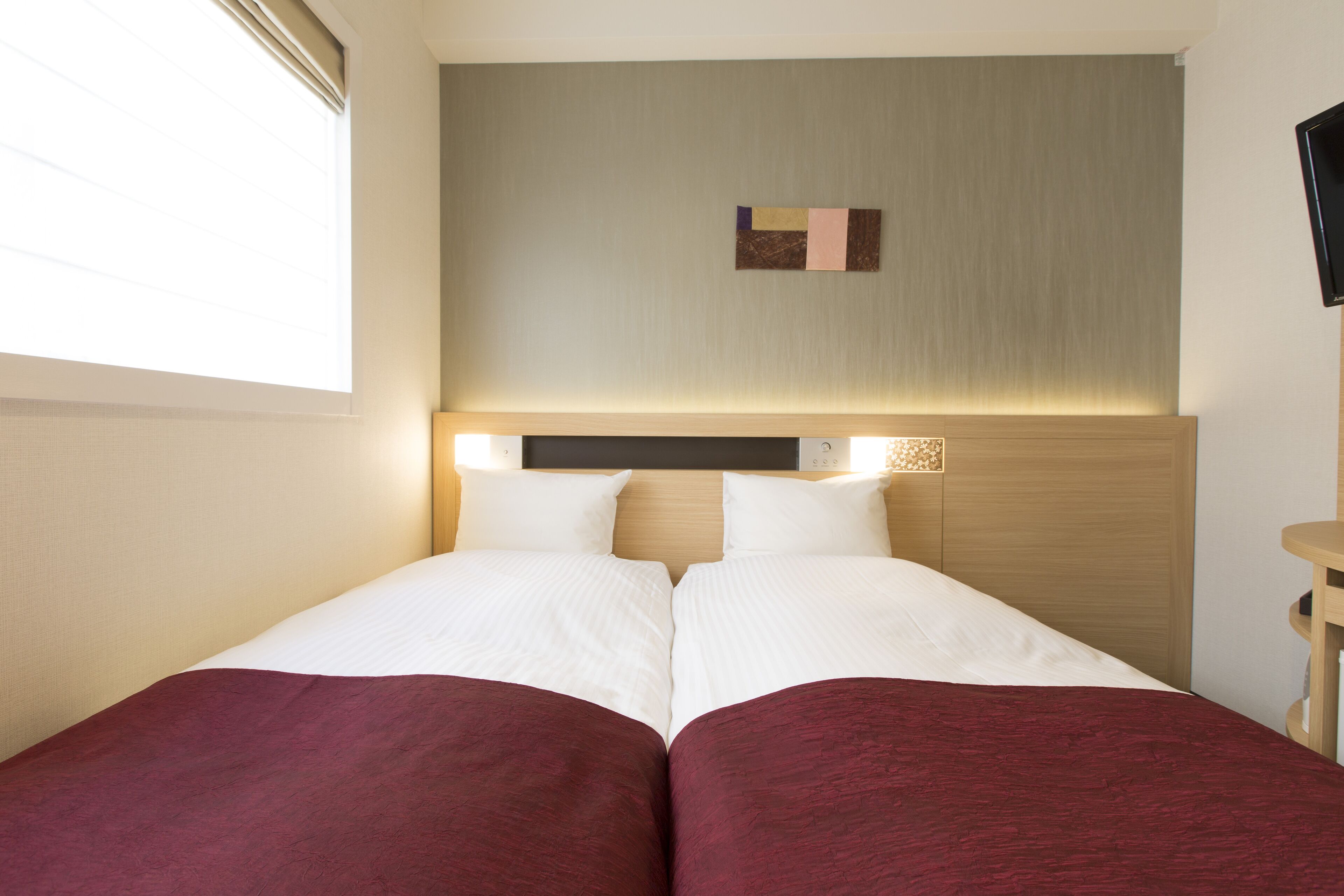Una habitación de hotel con una cama, cabecera, televisor montado en la pared y una ventana.