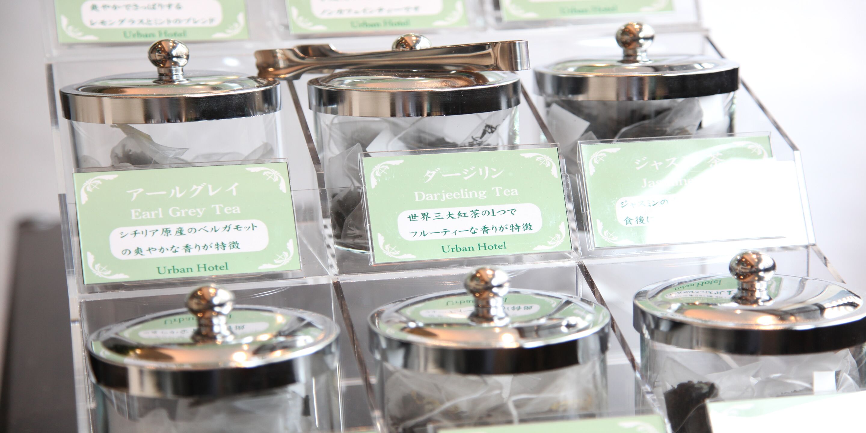 Une présentation de distributeurs de thé, chacun étant accompagné d’une étiquette indiquant le type de thé qu’il contient, notamment du thé Earl Grey et du thé Darjeeling, dans un hôtel urbain.
