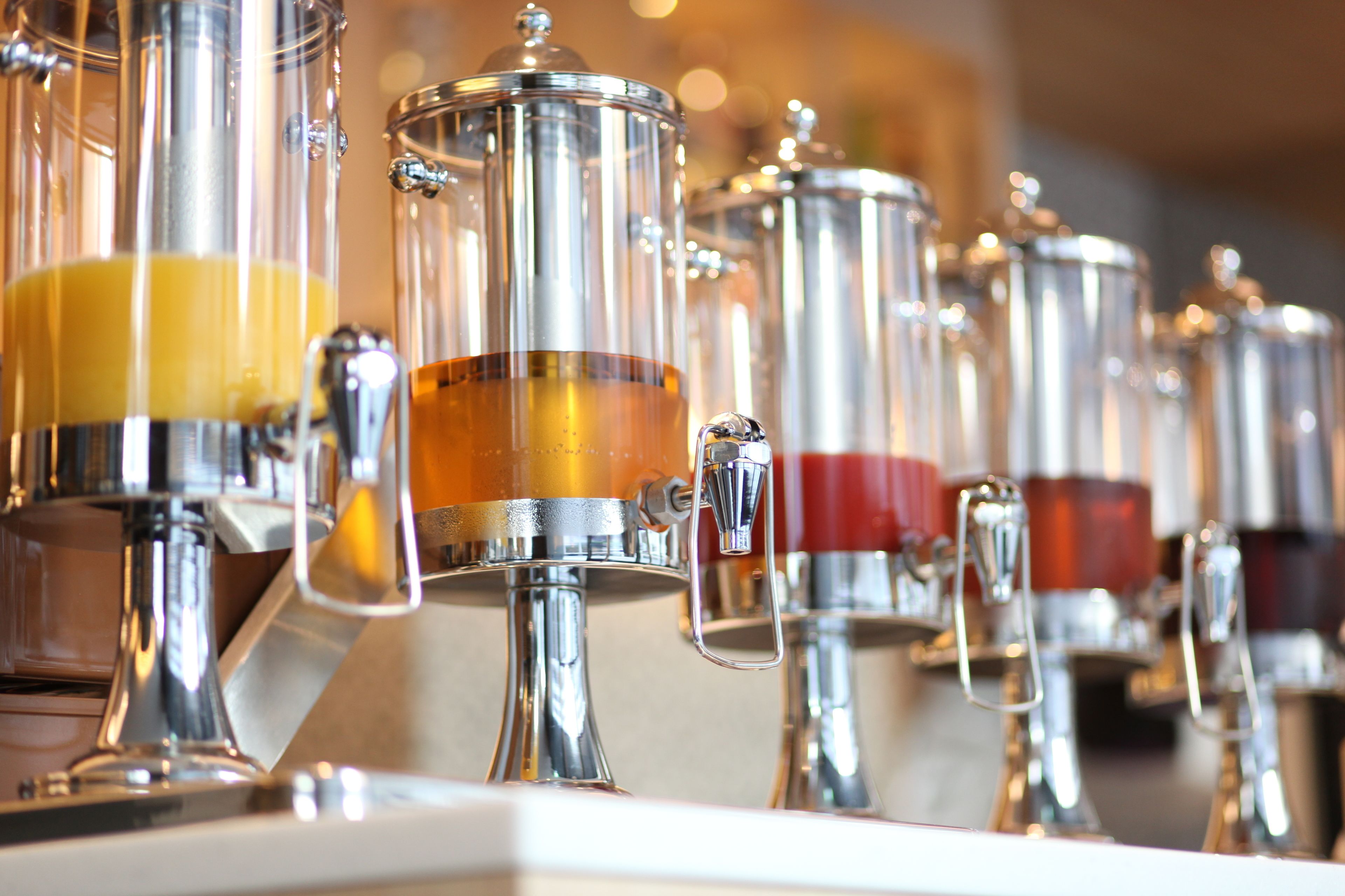 A row of stainless steel beverage dispensers with spouts.