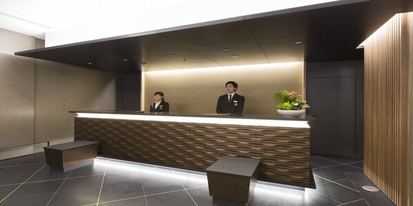 A reception desk with a modern design, two staff members, and a potted plant. - Urban Hotel Kyoto Nijo Premium (Kyoto)