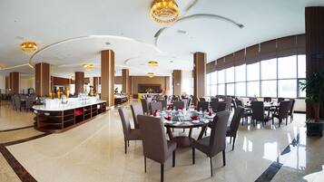 A spacious hotel dining area with high ceilings, large windows, and modern chandeliers.