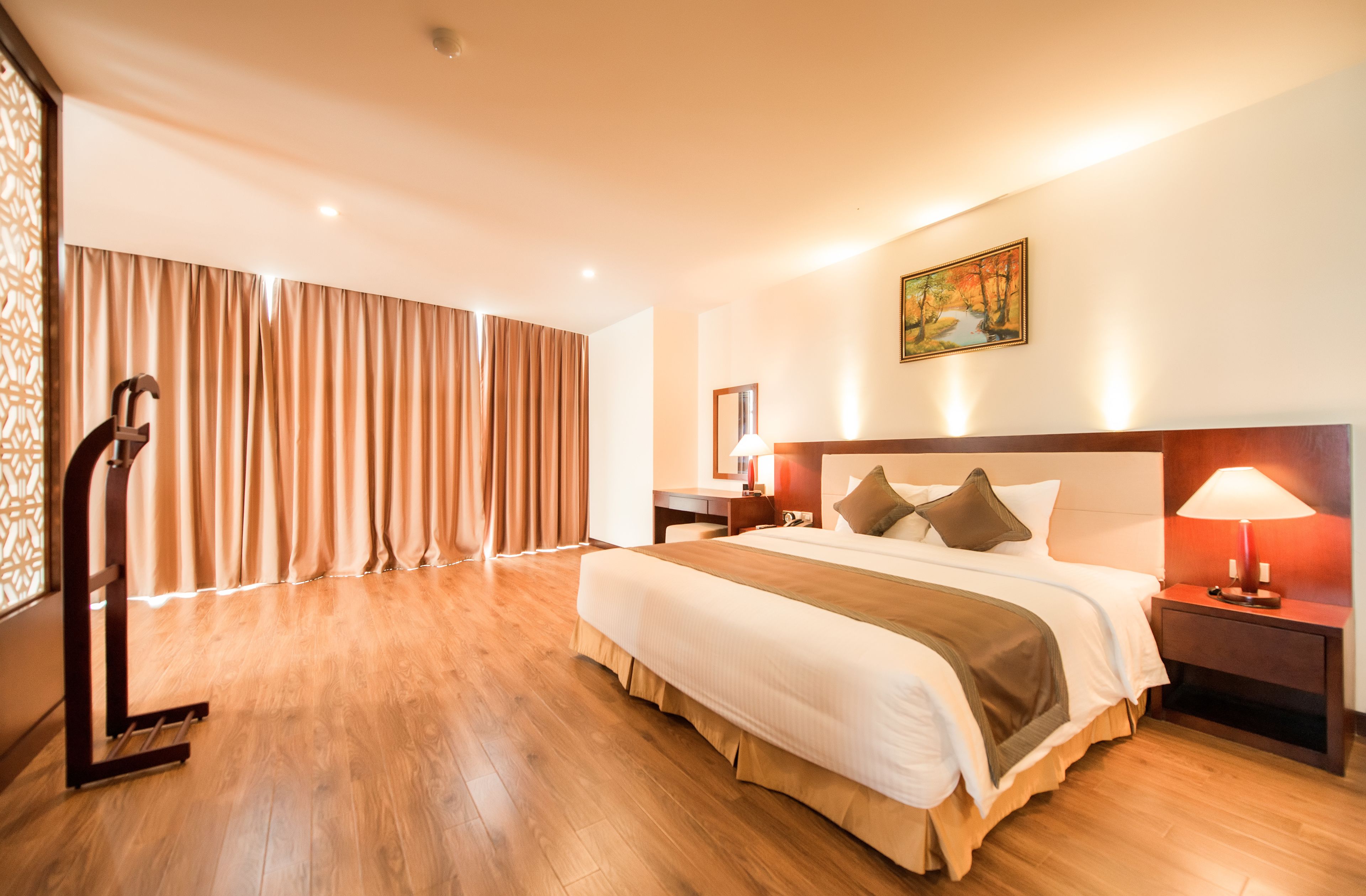 Habitación de hotel con una cama grande, un escritorio, una silla, una mesita de noche y un cuadro en la pared.