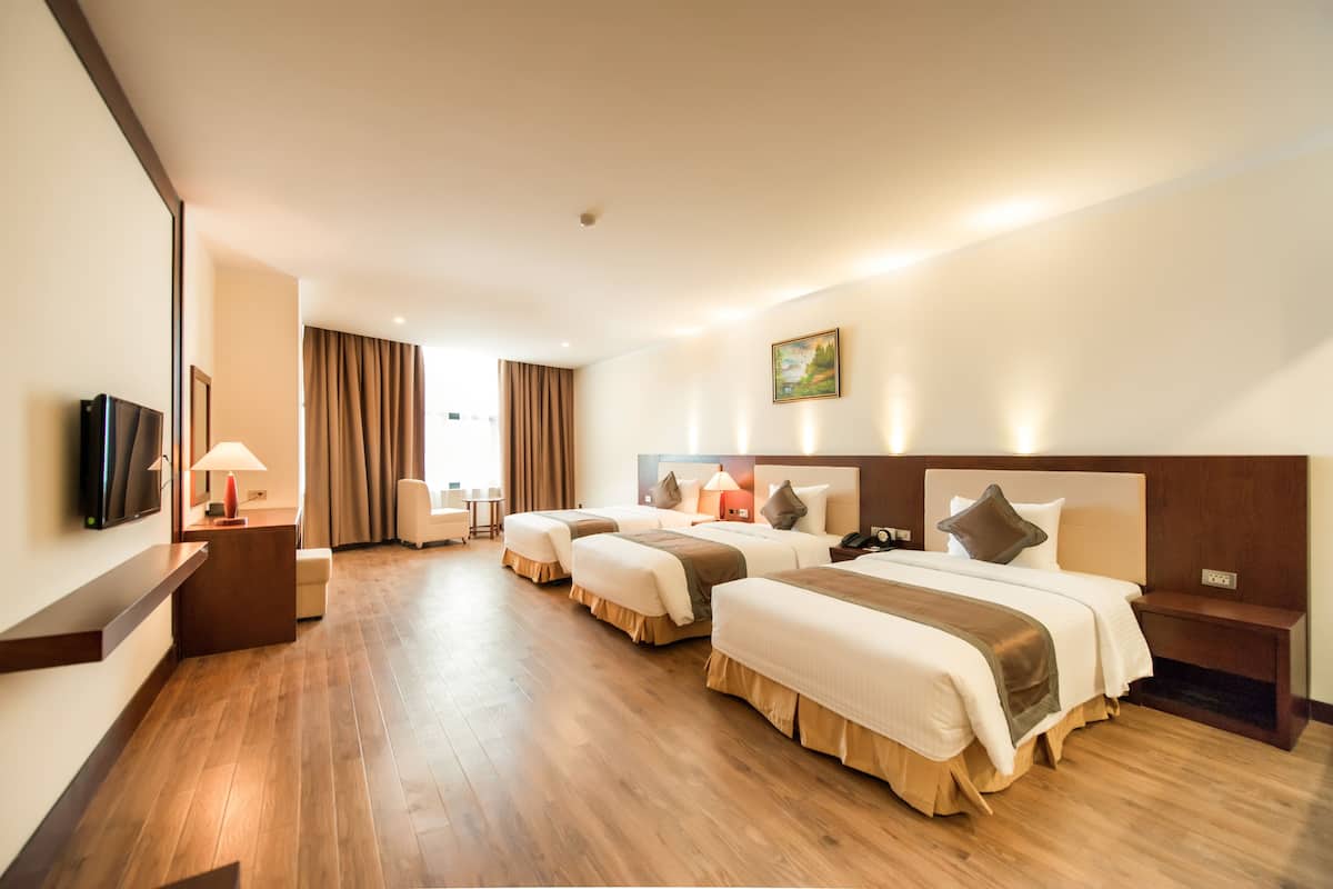 A hotel room with three beds, a TV, a desk, and a chair.