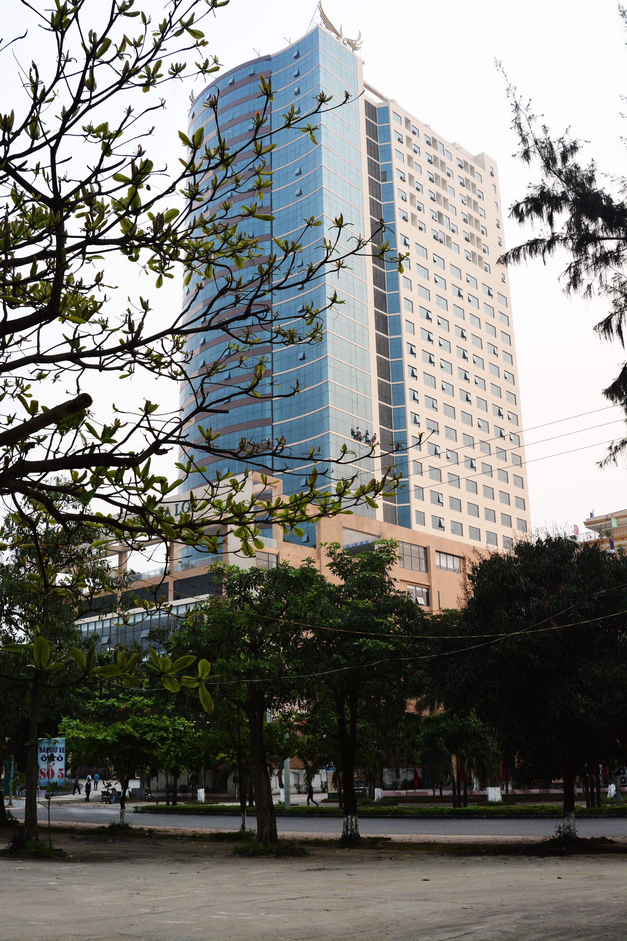 A tall building with a modern glass facade, surrounded by trees and a paved area.