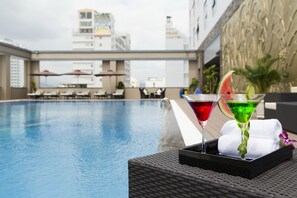 Zona junto a la piscina con una mesa de bar, dos cócteles y una toalla.