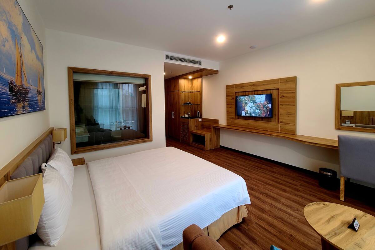 A hotel room with a large bed, a TV mounted on the wall, a wooden desk, and a window with a view.