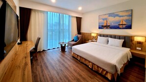 Habitación de hotel con una cama grande, un escritorio con silla, televisión, un cuadro de un velero y una ventana con cortinas.