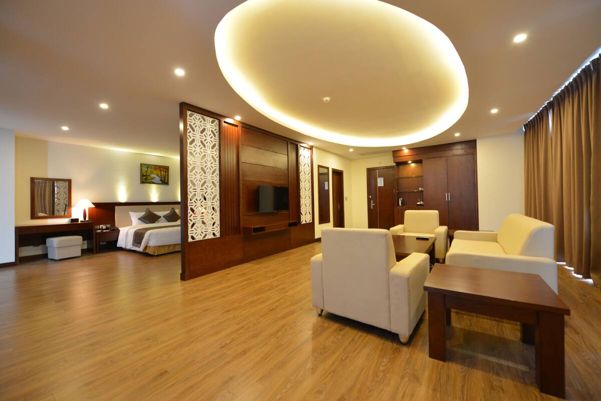 A modern hotel room with a wooden floor, a large bed, a TV, a sofa, and a coffee table.