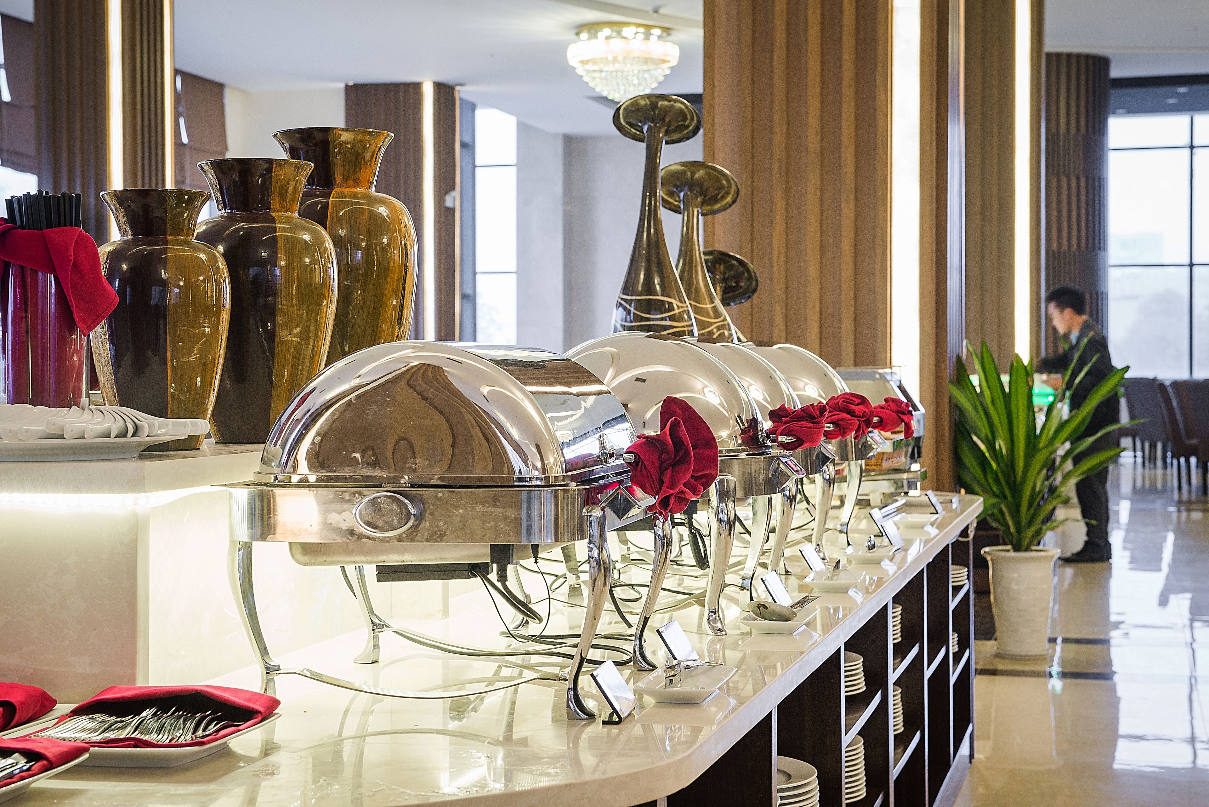 A buffet setup with multiple serving stations, a variety of glassware, and a potted plant.