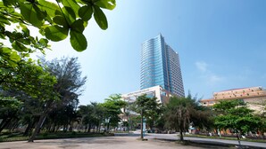 Un moderno edificio de gran altura con fachada de vidrio, rodeado por un parque arbolado y un cielo despejado.