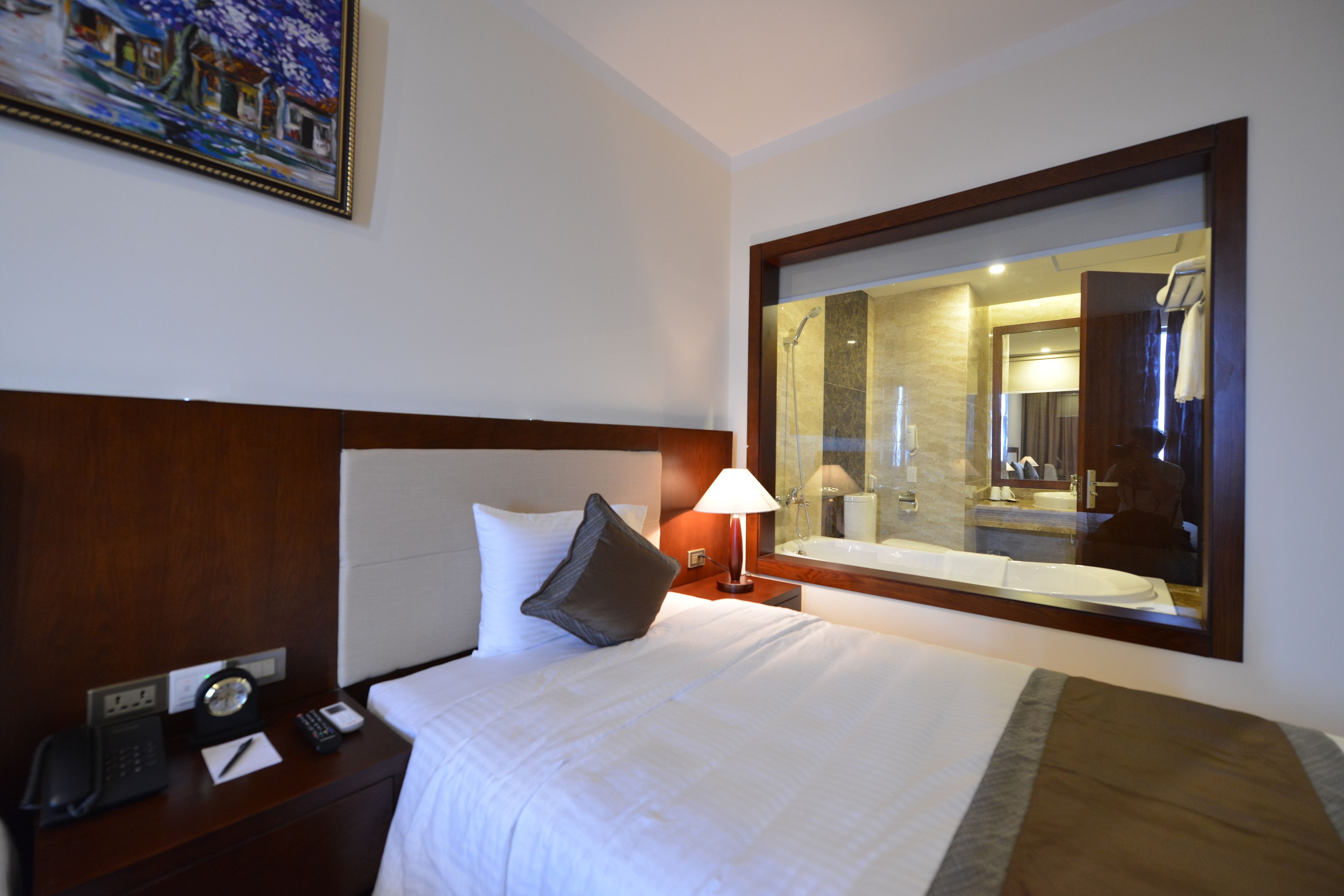 Habitación de hotel con una cama grande, una mesita de noche con lámpara, teléfono y un cuadro en la pared.