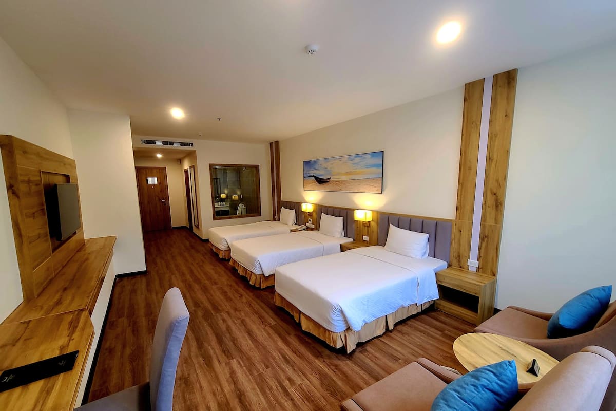 A hotel room with two beds, a TV, a wooden desk, a sofa, and a painting on the wall.