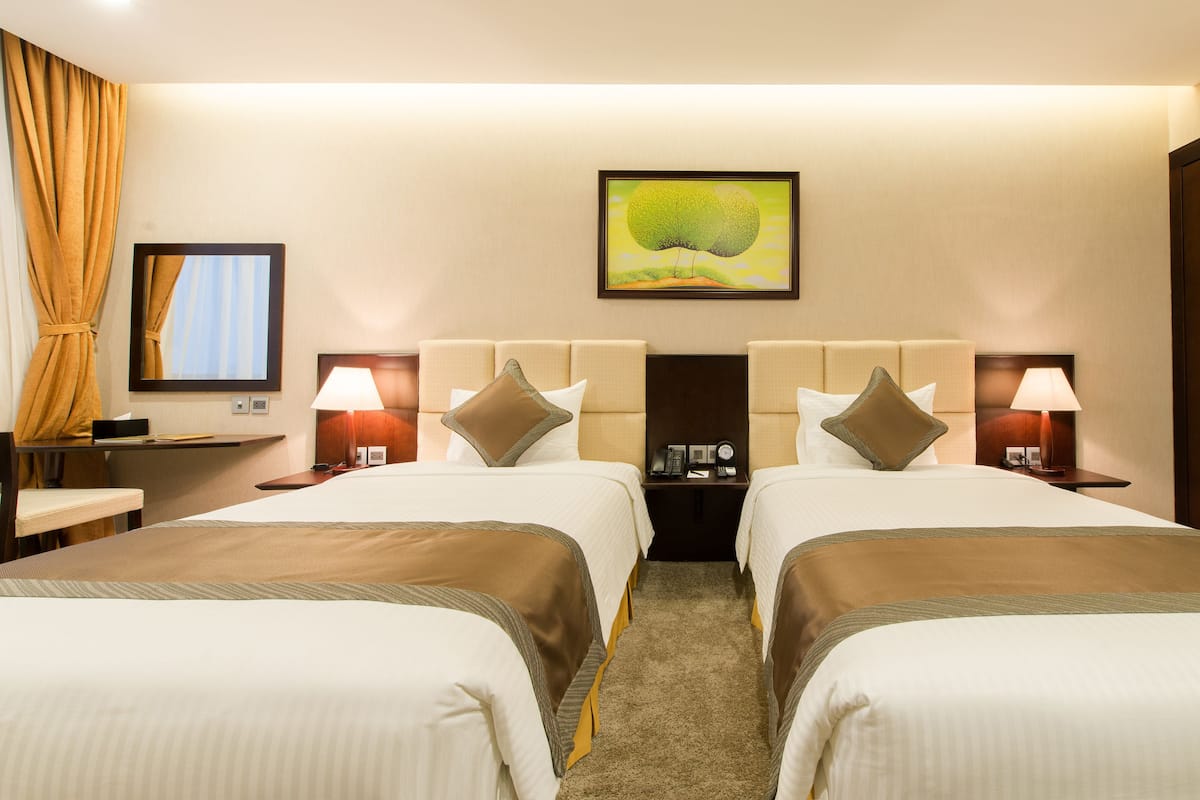 A hotel room with two beds, a large painting above the beds, and a television on the left wall.