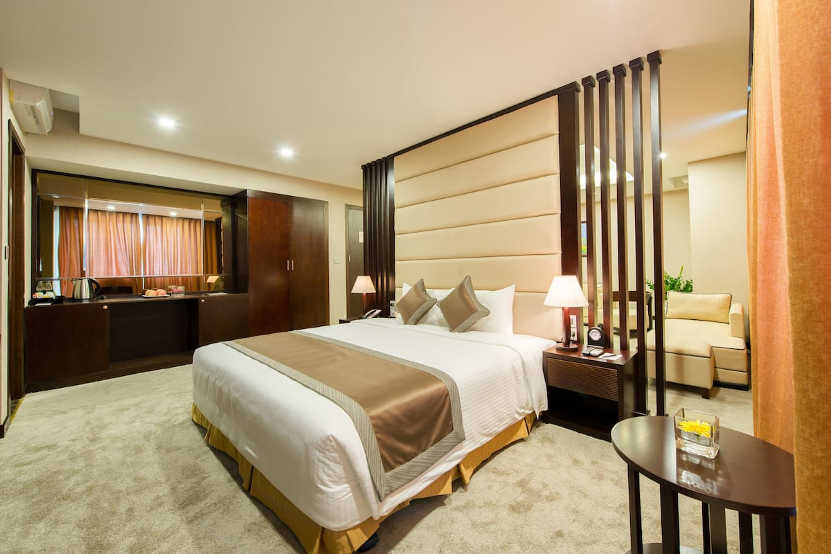A hotel room with a large bed, a desk, a chair, a nightstand, and a small table.