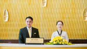 A reception desk with a sign reading "LE TÃN RECEPTION" and a bouquet of yellow flowers. - Muong Thanh Hanoi Centre Hotel (Hanoi)
