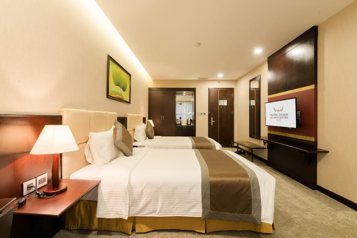 A hotel room with two beds, a desk with a lamp, a TV, and a framed picture on the wall.