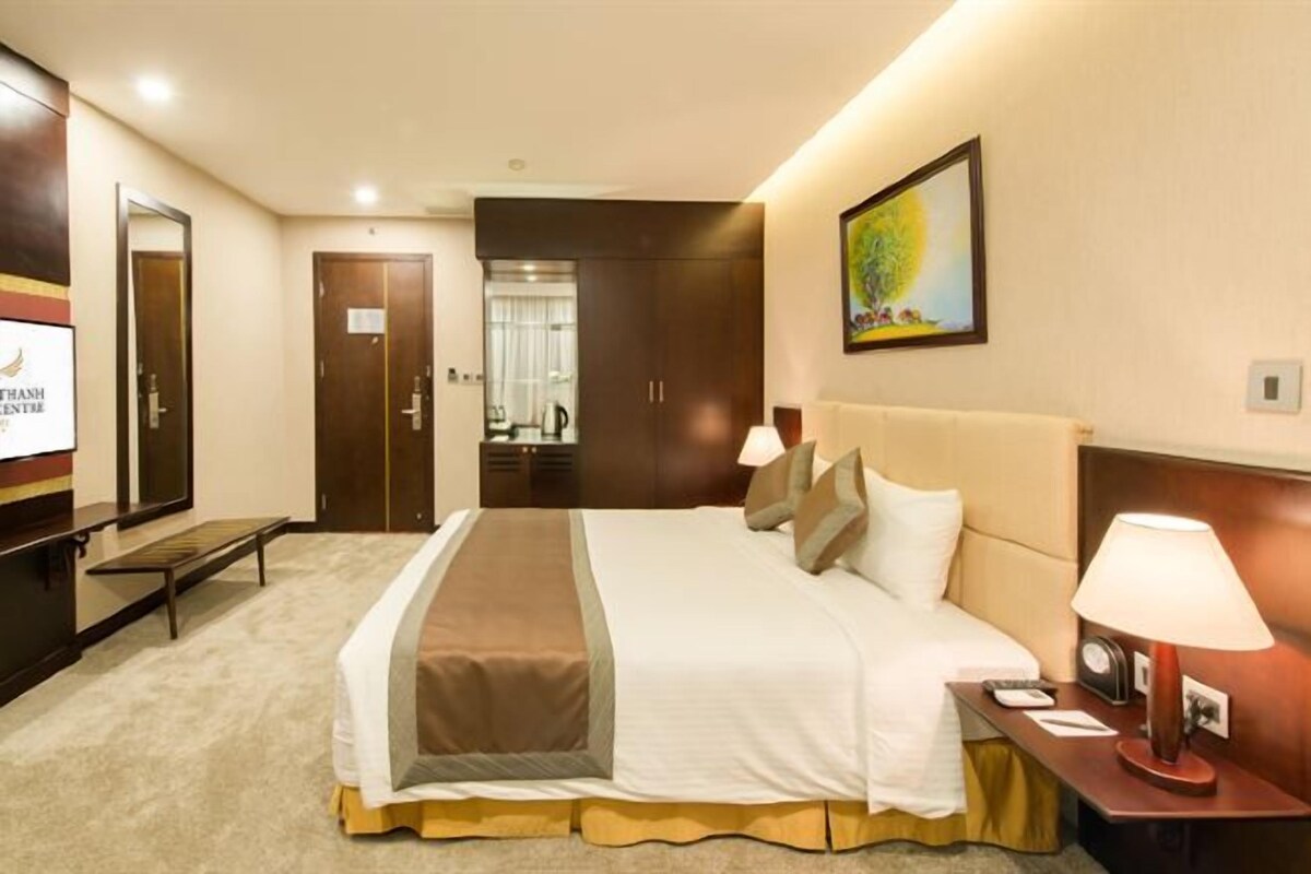 A hotel room with a large bed, a bedside table with a lamp, a TV, and a wardrobe.