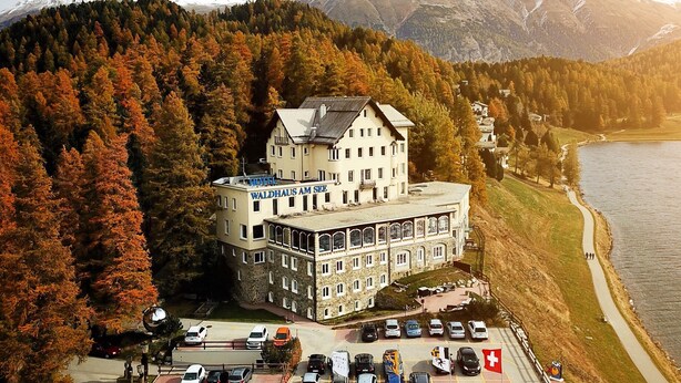 Un hotel con un edificio central rodeado de un estacionamiento y un lago.