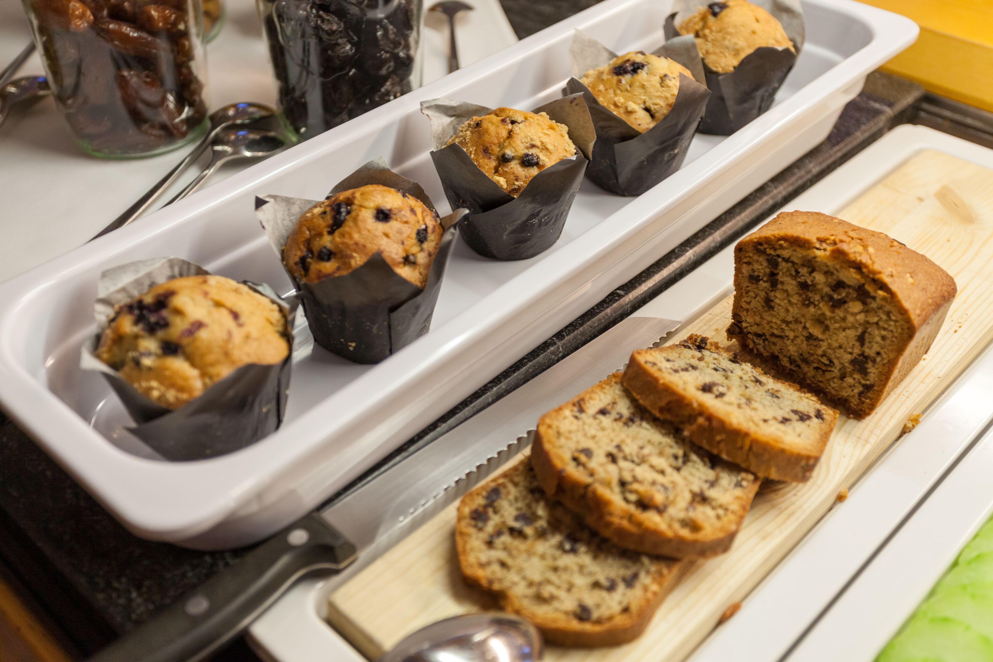 Muffins in paper cups on a tray and sliced bread on a cutting board.
