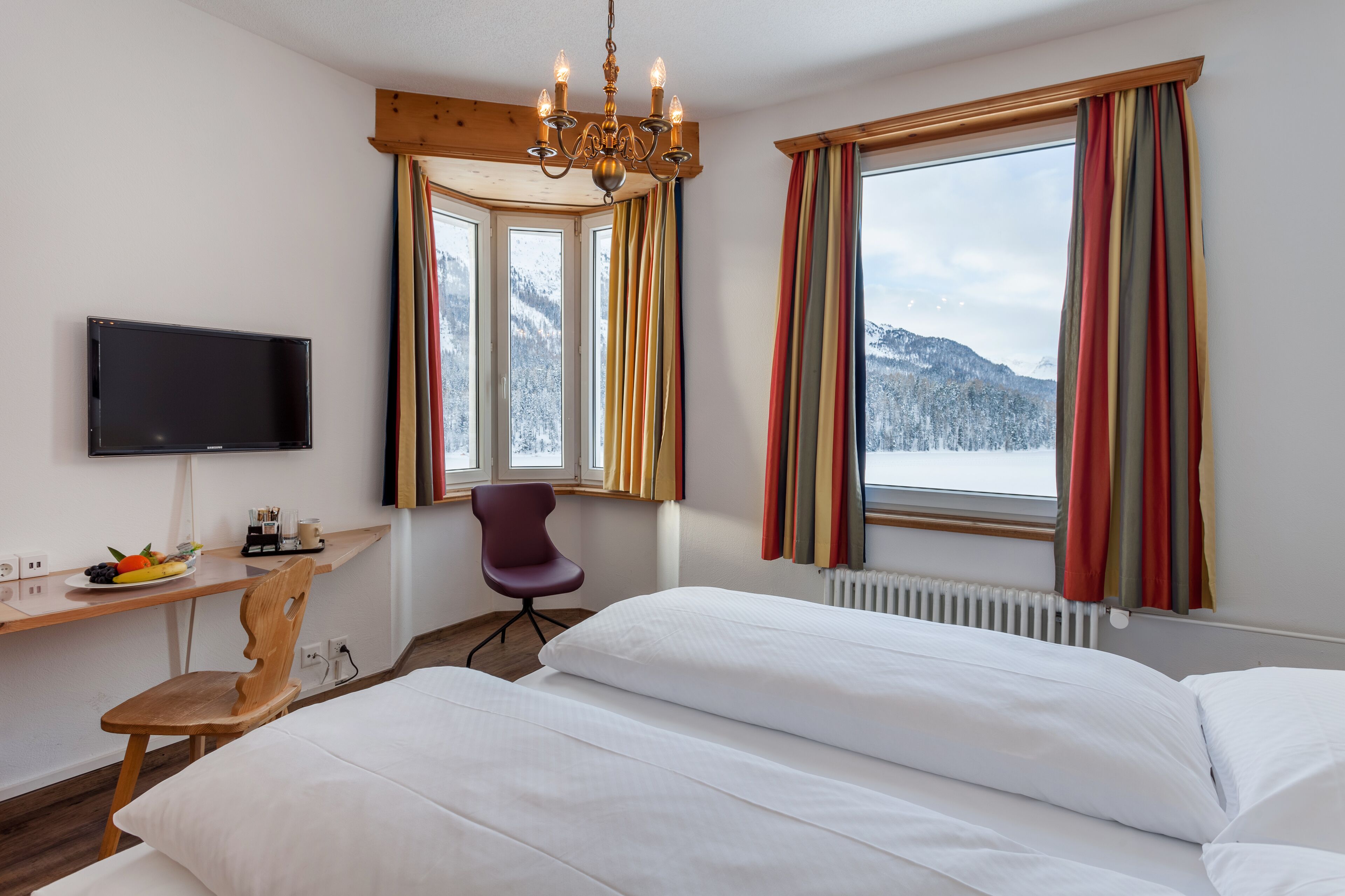 A hotel room with a bed, a desk with a chair, a TV, and a window with curtains.