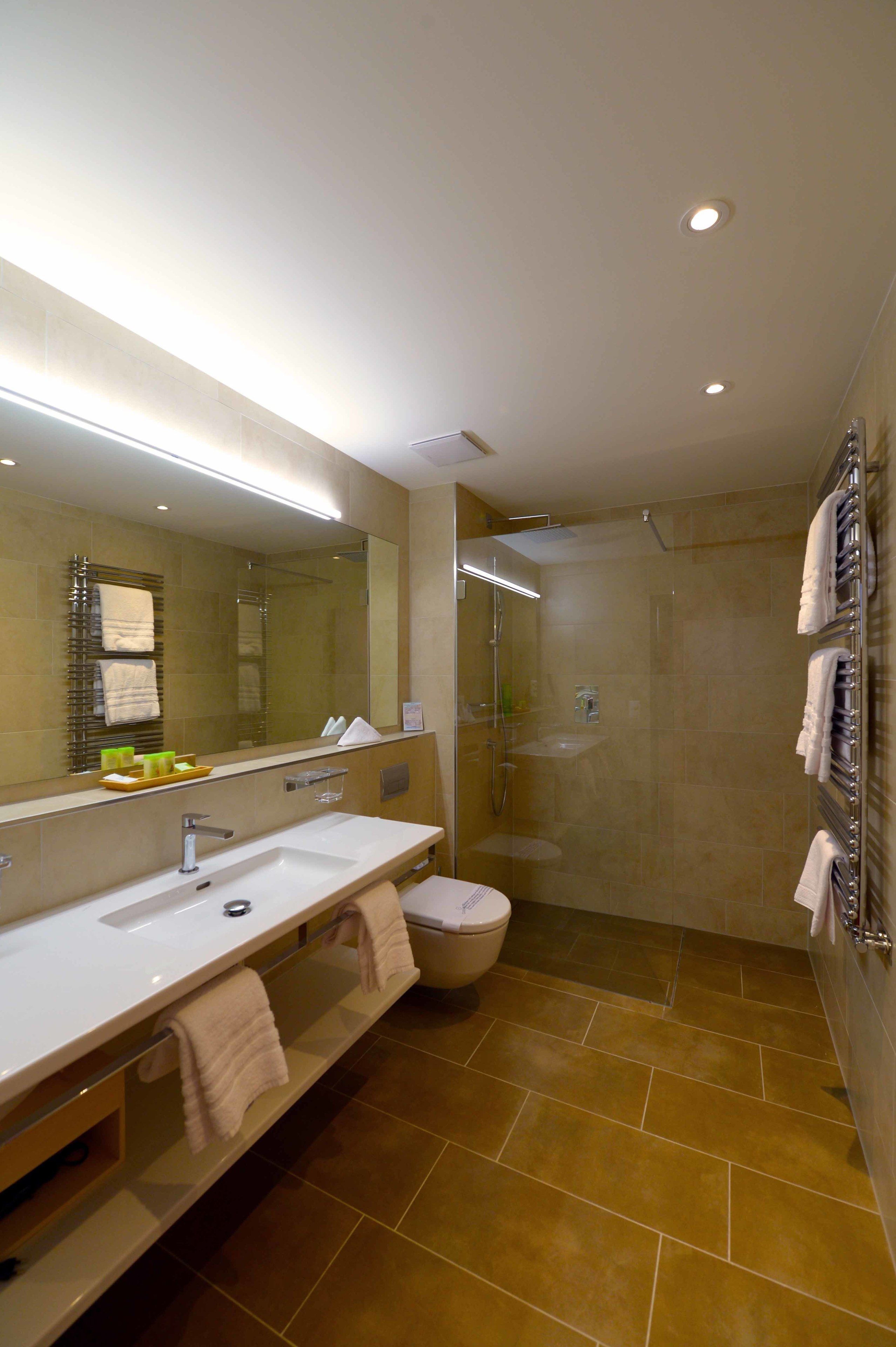 A modern bathroom with a large mirror, dual sinks, a shower, and a towel rack.