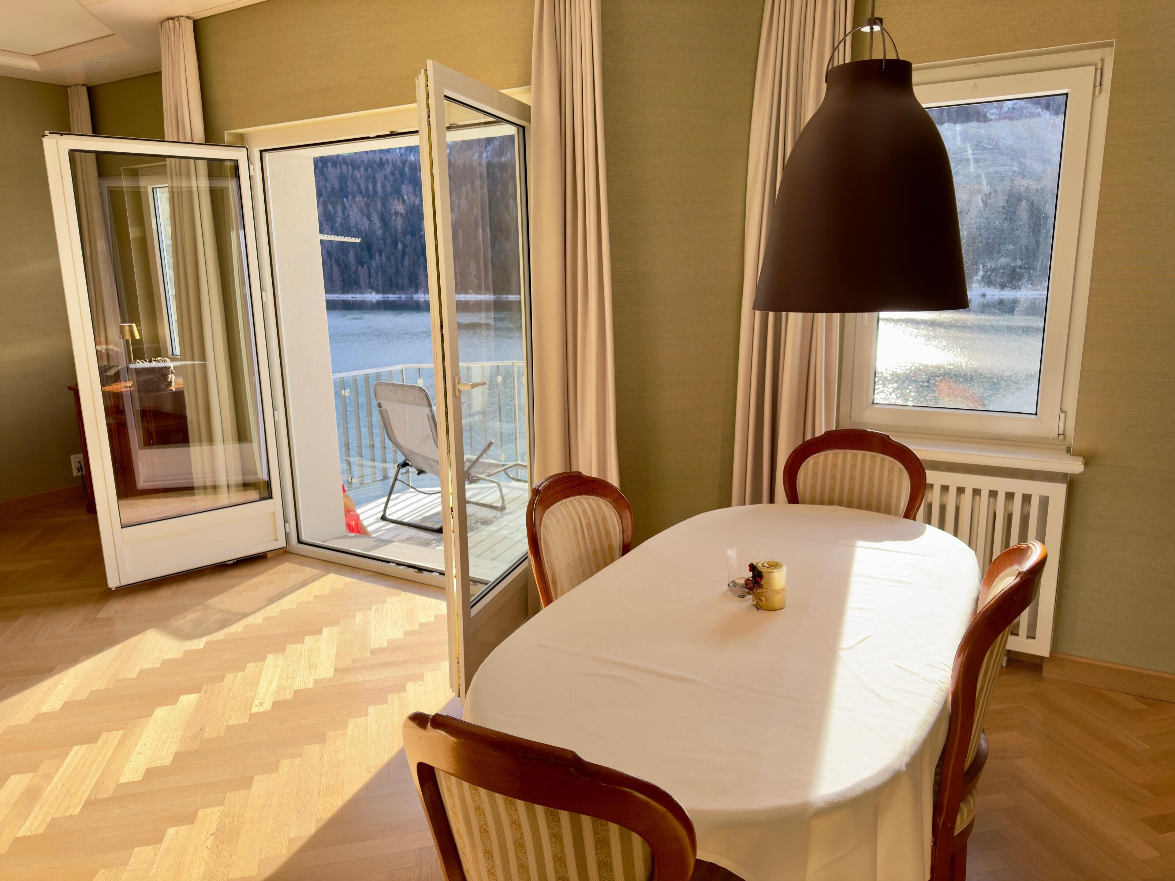 A dining area with a table, chairs, a pendant light, and a view of a snowy landscape through a glass door.