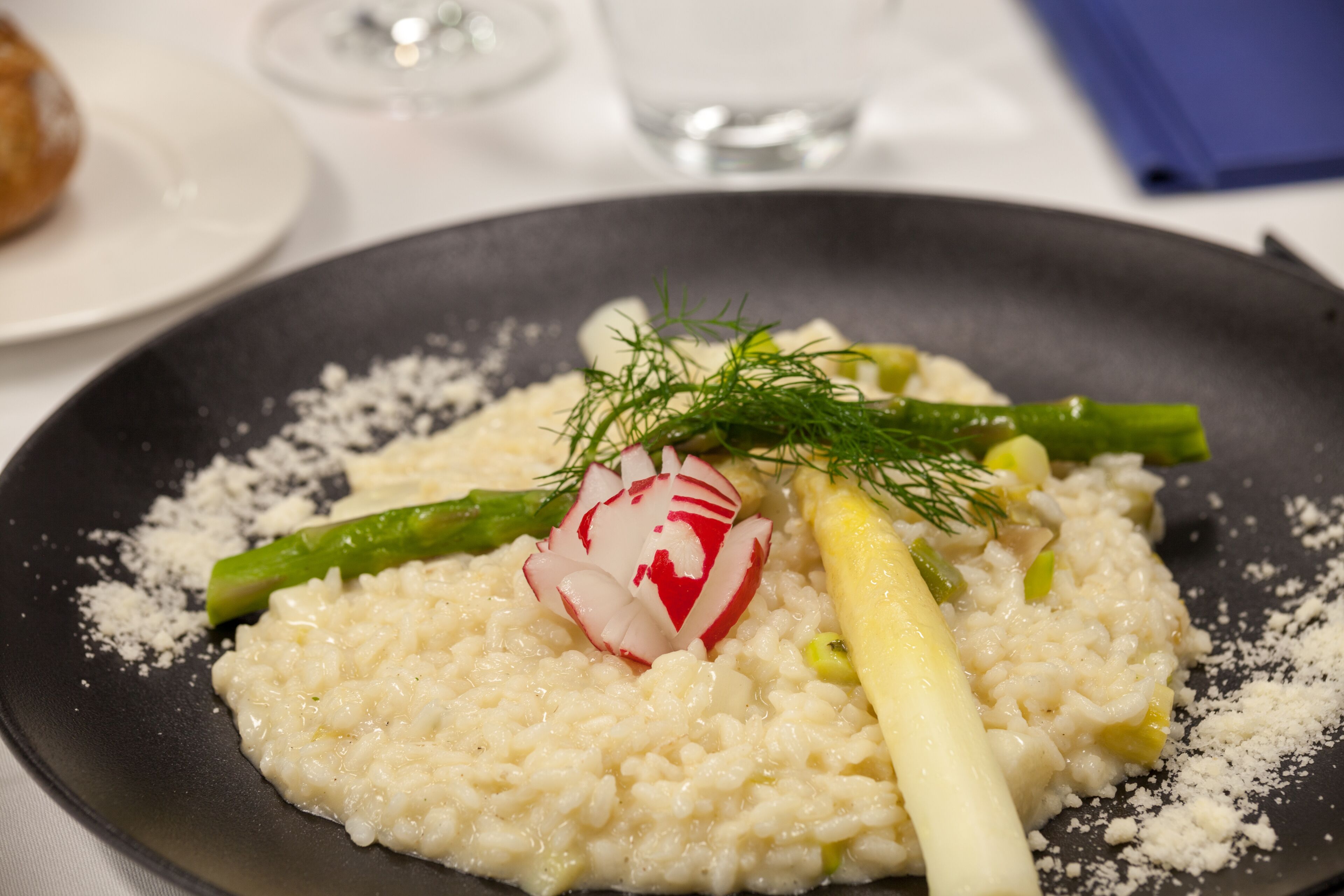 Un plato de risotto con espárragos, rábanos y adorno de eneldo.