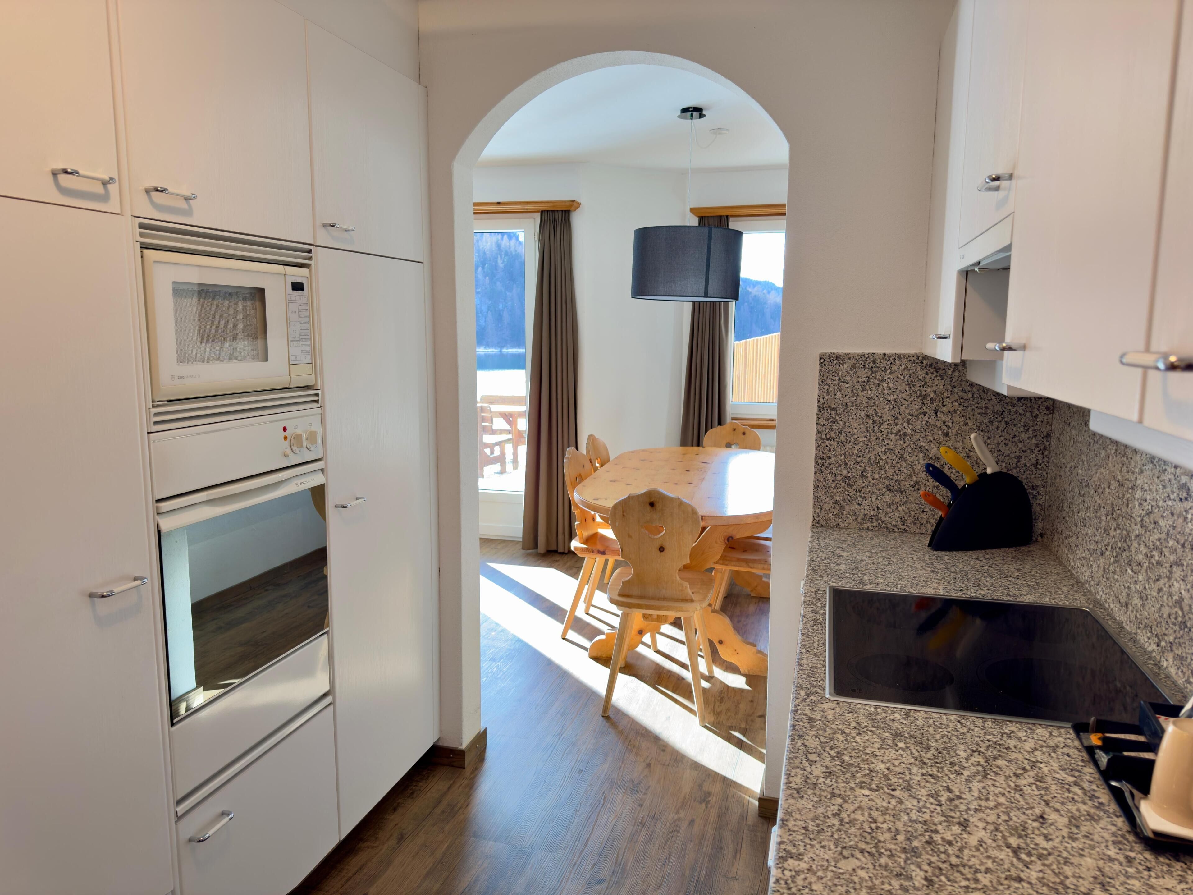 A modern kitchen with white cabinets, a granite countertop, and a dining area with wooden furniture.