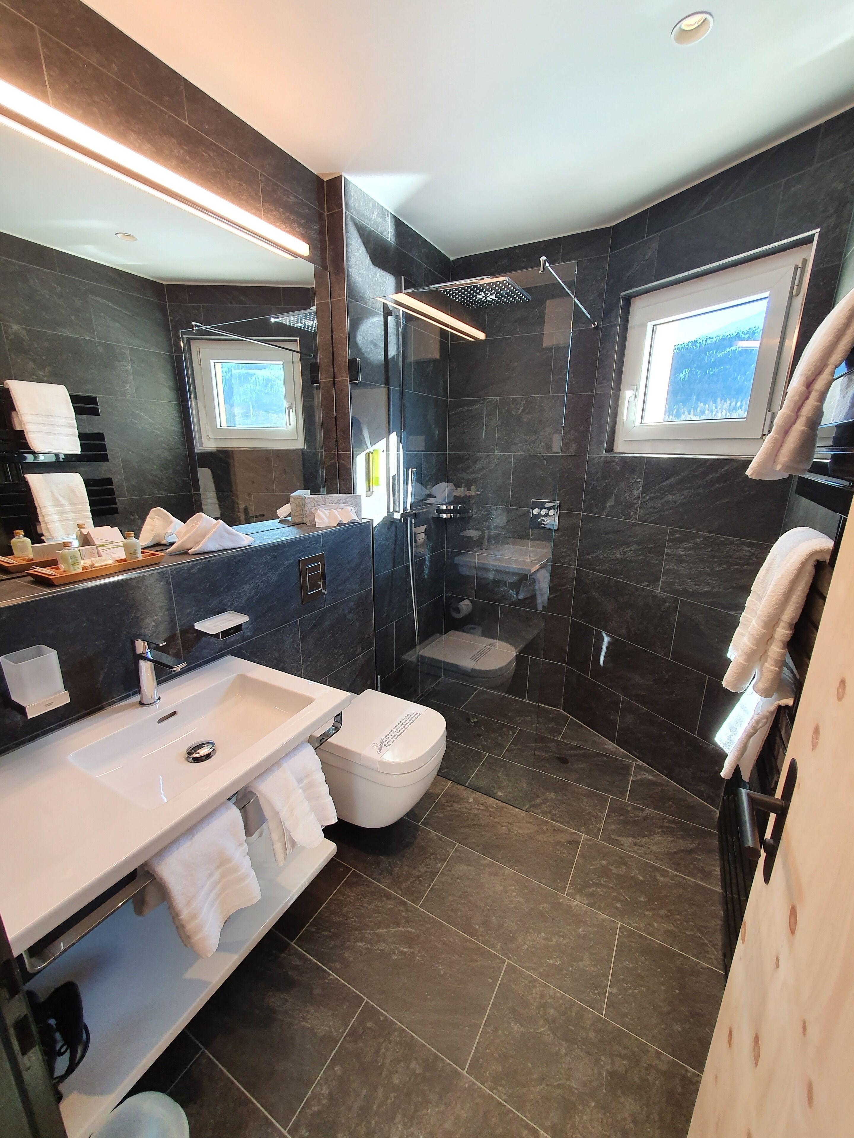 Een moderne badkamer met een douchekabinet van glas, een grote spiegel en een raam voor natuurlijk licht.