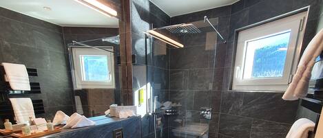 A modern bathroom with a glass-enclosed shower, a large mirror, and a window providing natural light.