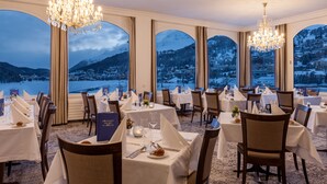 Un comedor con mesas dispuestas para una comida, ventanas amplias que ofrecen vistas a un paisaje nevado de montañas y candelabros que brindan iluminación.