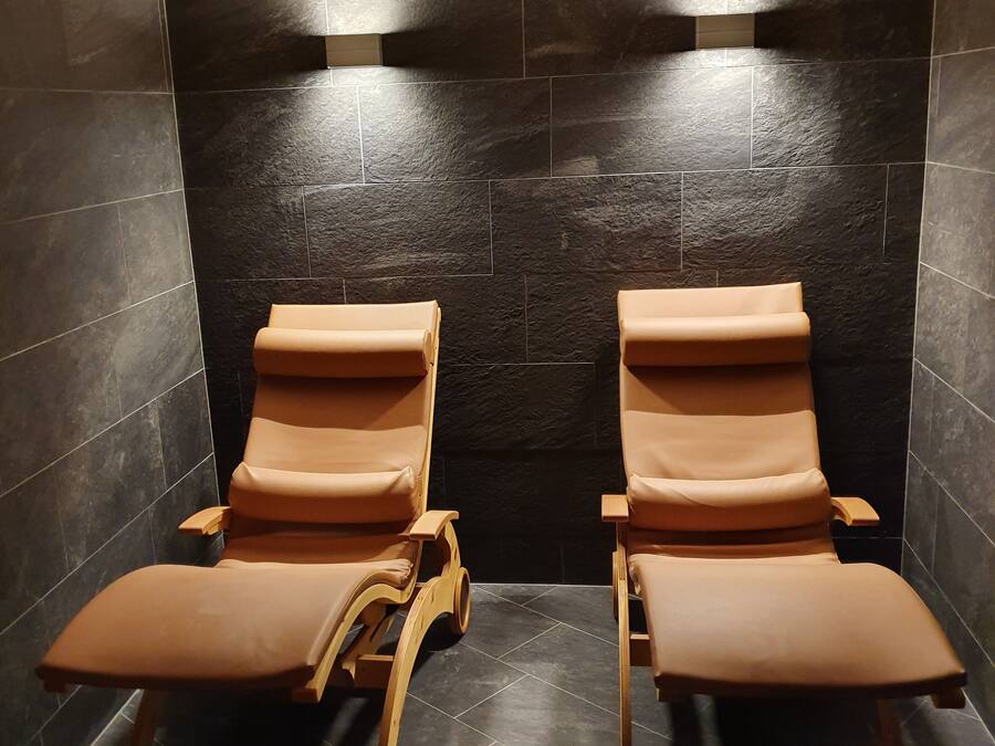 Un cuarto de spa con dos sillas de masaje de madera y paredes de piedra oscura.