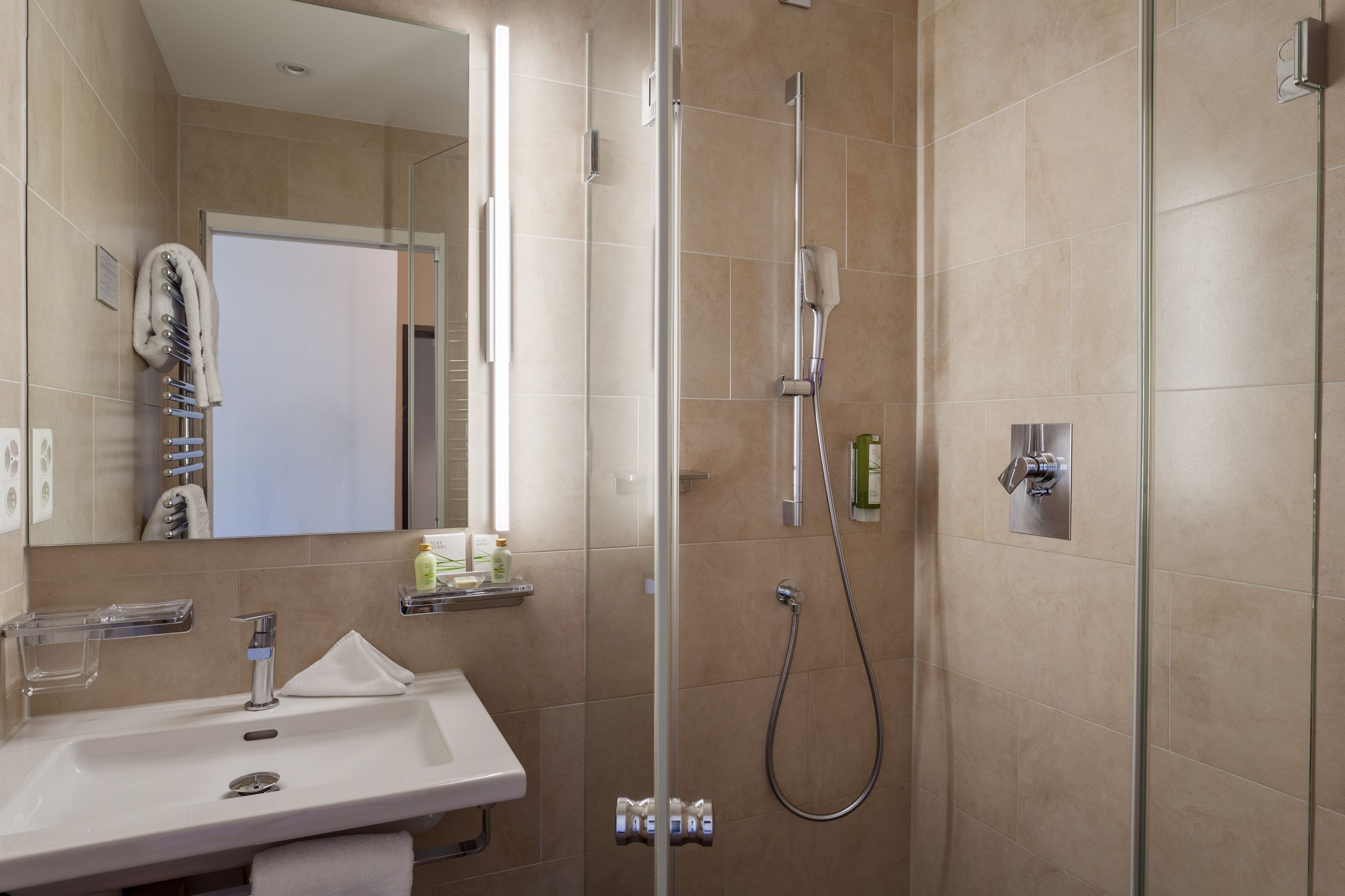A modern bathroom with a glass-enclosed shower, a sink with a mirror, and a towel rack.