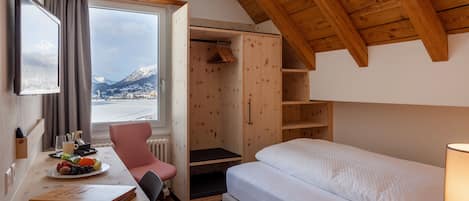Una camera da letto con un letto, una scrivania con un portatile, una sedia, una finestra vista montagne e un soffitto in legno.